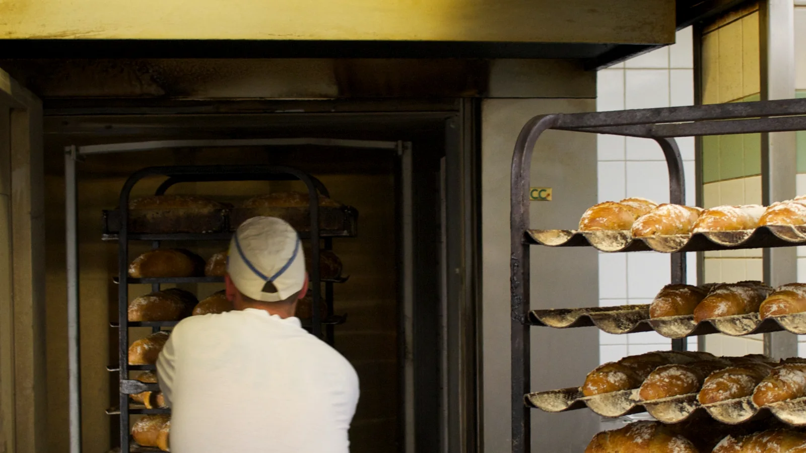Baecker schiebt Brot in einen industriellen Backofen in einer gewerblichen Backstube