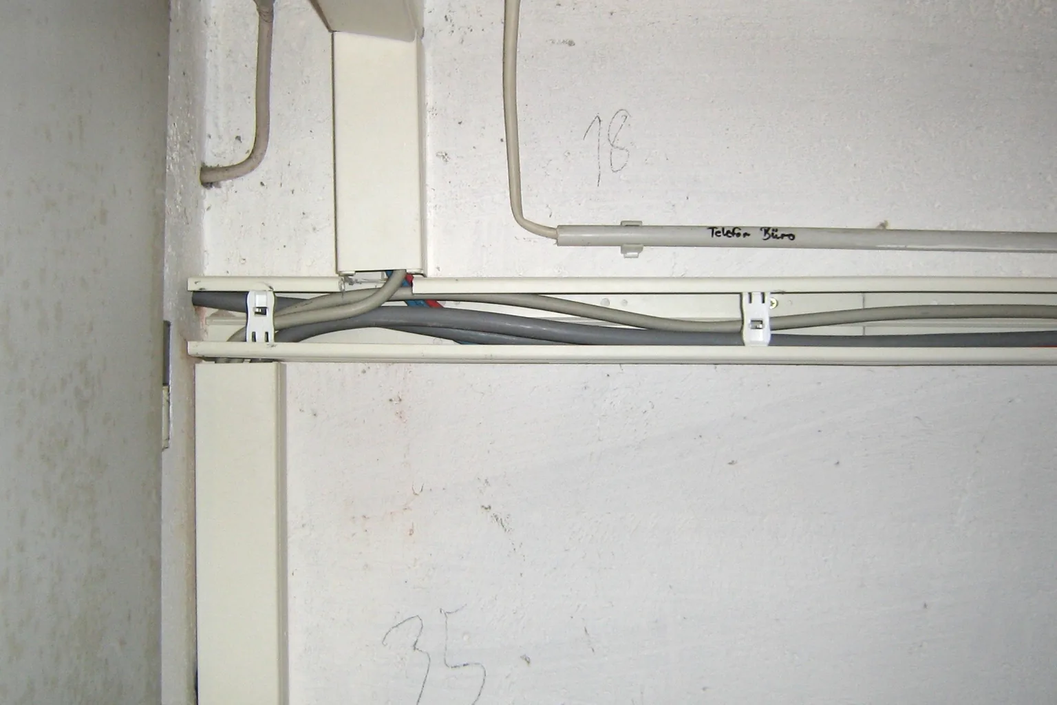Teilweise geöffneter Kabelkanal einer Elektroinstallation in einem Kellerraum; Leitungen sind im Kanal sichtbar