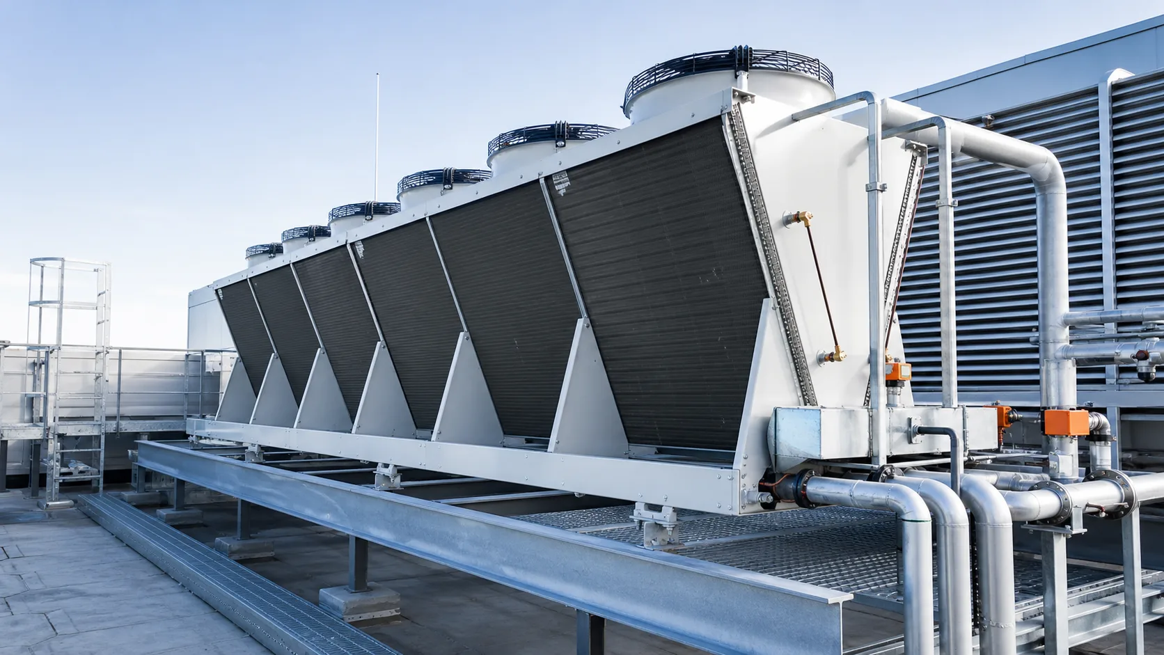 Großer Rückkühler auf dem Dach eines Industriegebäudes mit mehreren Ventilatorsegmenten und angeschlossener Rohrleitung