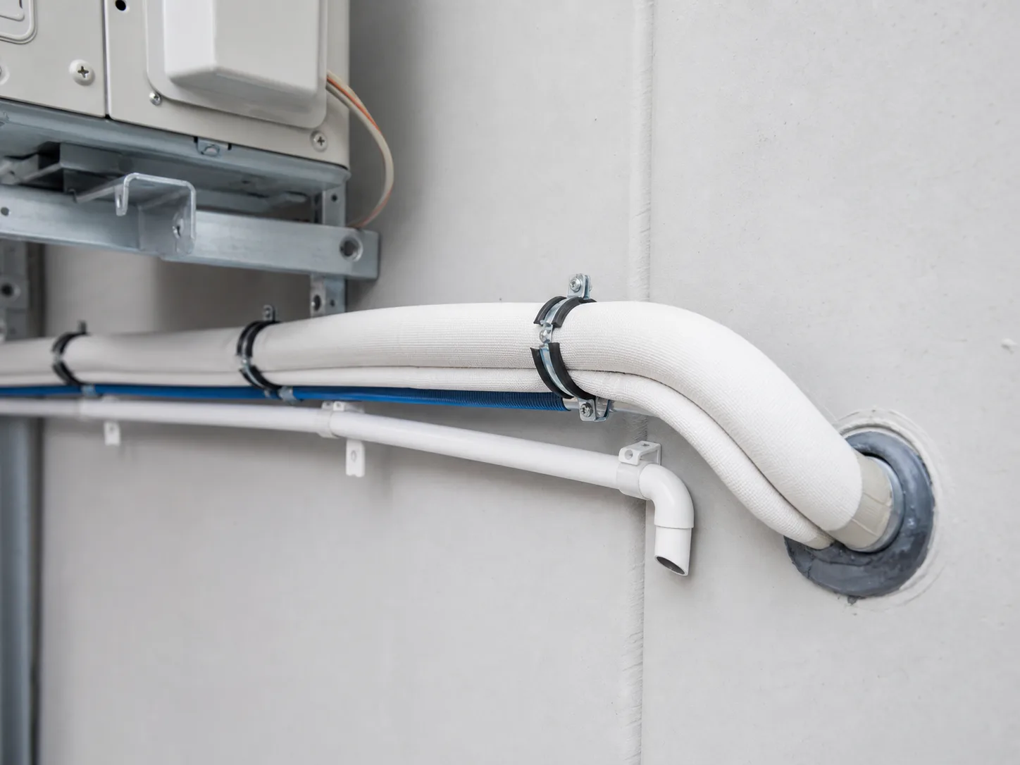 Sauber geführte, gedämmte Kältemittelleitungen und Kondensatleitung nach einer Wanddurchführung an einer Split-Klimaanlage